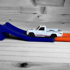 Hot Wheels Track Compatible Jump in use, showcasing a car speeding up the ramp and flying through the air. Custom Hot Wheels jump designed for tighter, shorter jumps, enhancing the obstacle course experience for kids. Made from eco-friendly PLA plastic by a small business in the USA