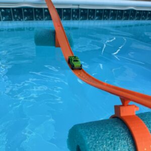 Green Hot Wheels truck racing on an orange floating track system attached to blue pool noodles in a backyard swimming pool, demonstrating the Pool Track for Hot Wheels in action